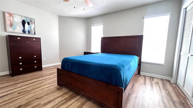 bedroom featuring baseboards, light wood-style floors, a ceiling fan, and a textured ceiling