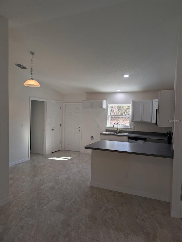 kitchen with visible vents, a peninsula, a sink, pendant lighting, and dark countertops