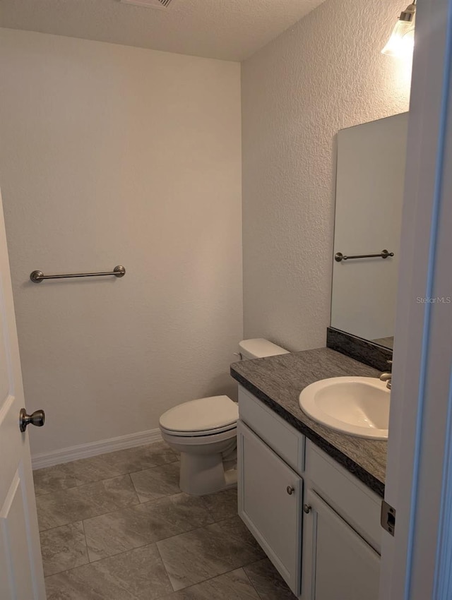 half bath with toilet, vanity, baseboards, and a textured wall