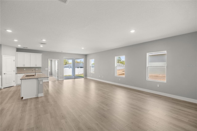 unfurnished living room featuring baseboards, light wood-style floors, a textured ceiling, and recessed lighting