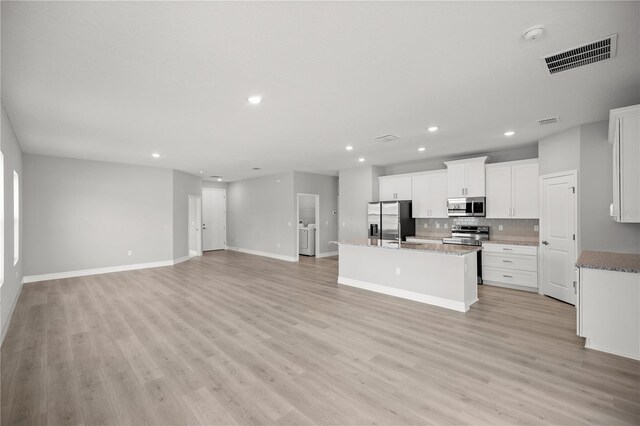 kitchen with visible vents, appliances with stainless steel finishes, an island with sink, open floor plan, and backsplash