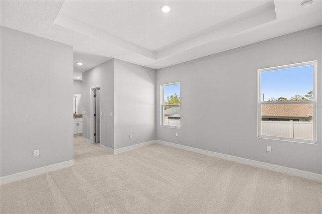 empty room with a raised ceiling, light carpet, baseboards, and recessed lighting