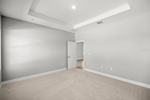 spare room with a tray ceiling, baseboards, light colored carpet, and visible vents