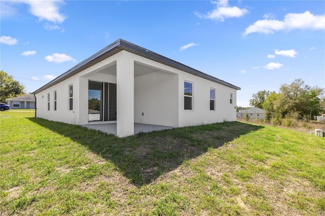 rear view of property featuring stucco siding, a patio area, and a yard