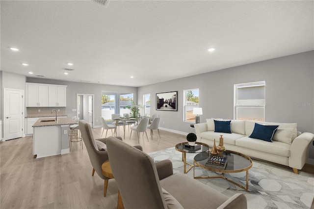 living room with baseboards, a textured ceiling, recessed lighting, and light wood finished floors