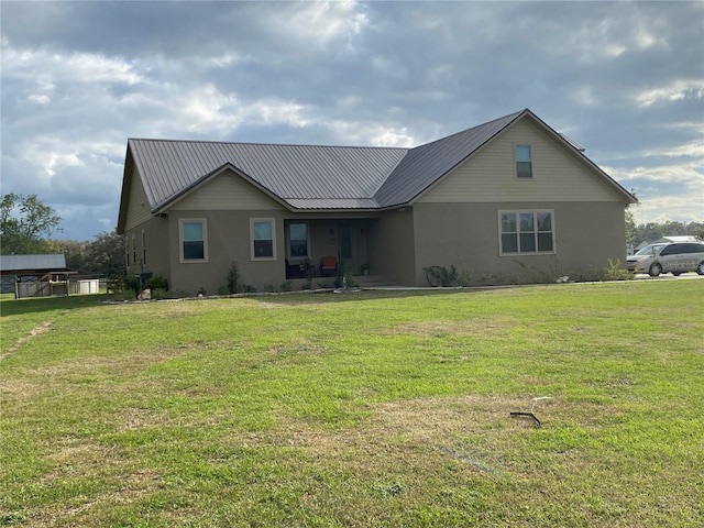 back of property with a lawn, metal roof, and stucco siding