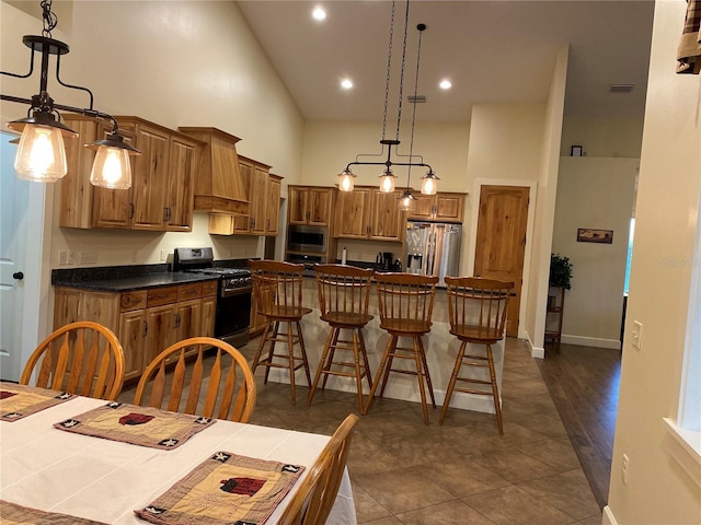 kitchen with dark countertops, a kitchen island, a kitchen bar, appliances with stainless steel finishes, and a towering ceiling