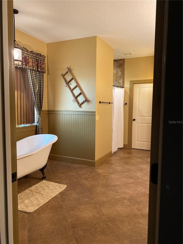 bathroom with wainscoting, a freestanding bath, a textured ceiling, and a shower with shower curtain