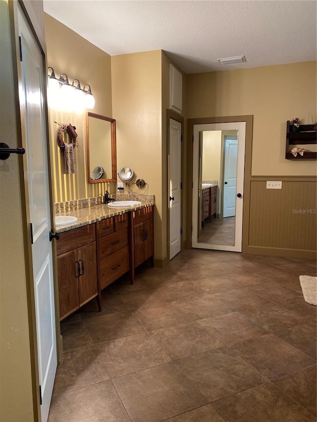 bathroom featuring visible vents, double vanity, wainscoting, a sink, and a textured ceiling