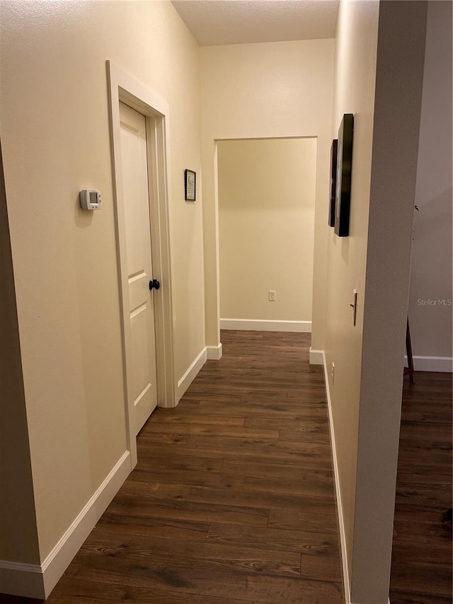 hallway featuring dark wood-type flooring and baseboards