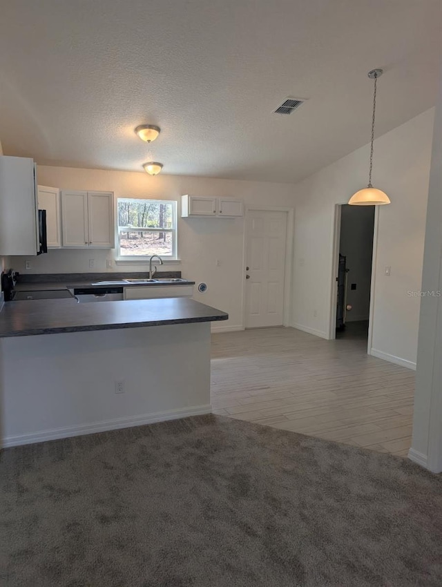 kitchen featuring visible vents, a peninsula, a sink, stove, and dark countertops