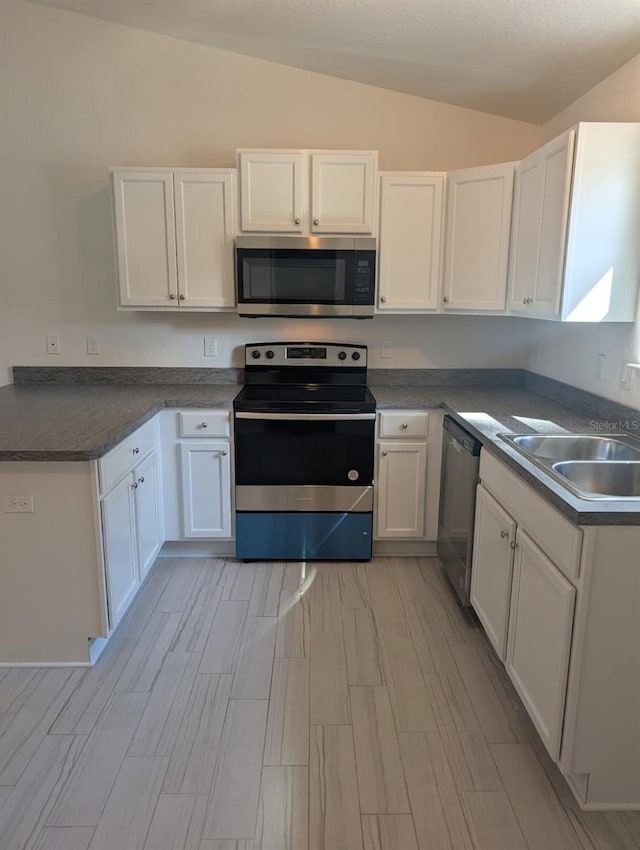 kitchen featuring a sink, dark countertops, appliances with stainless steel finishes, white cabinets, and lofted ceiling