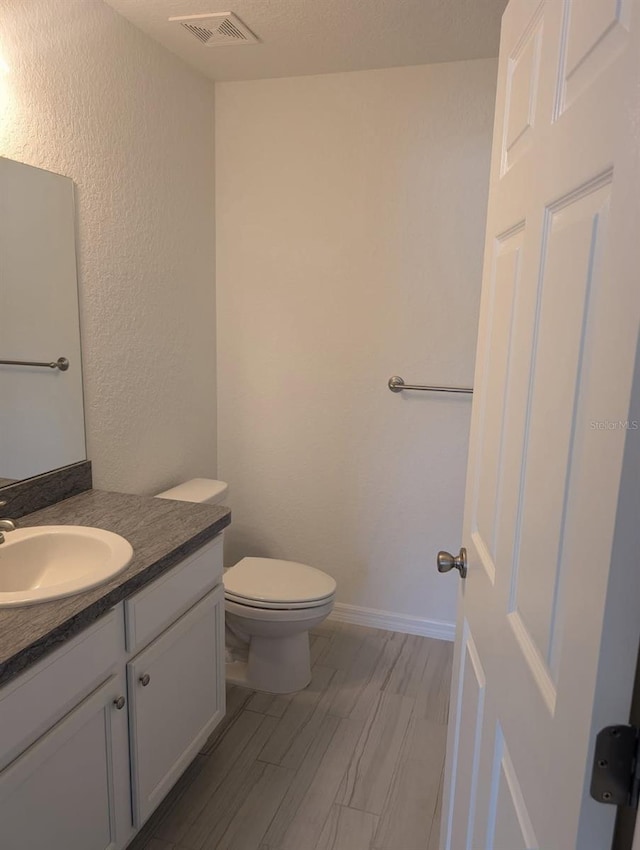 half bath with visible vents, baseboards, toilet, wood finished floors, and vanity