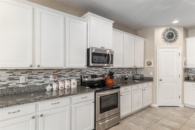 kitchen featuring dark stone counters, light tile patterned floors, decorative backsplash, appliances with stainless steel finishes, and white cabinetry