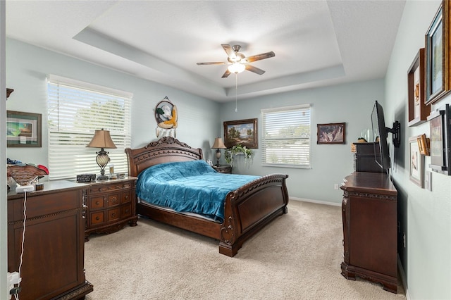 bedroom with light carpet, ceiling fan, baseboards, and a tray ceiling