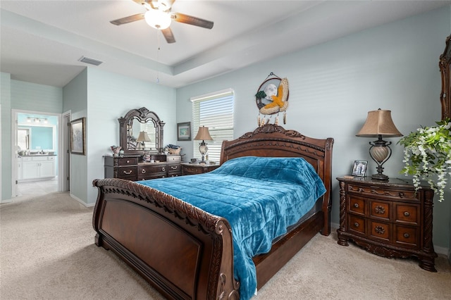 bedroom featuring baseboards, visible vents, ensuite bath, a tray ceiling, and light carpet