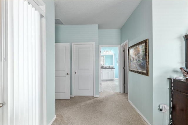 hall featuring visible vents, light colored carpet, a textured ceiling, and baseboards