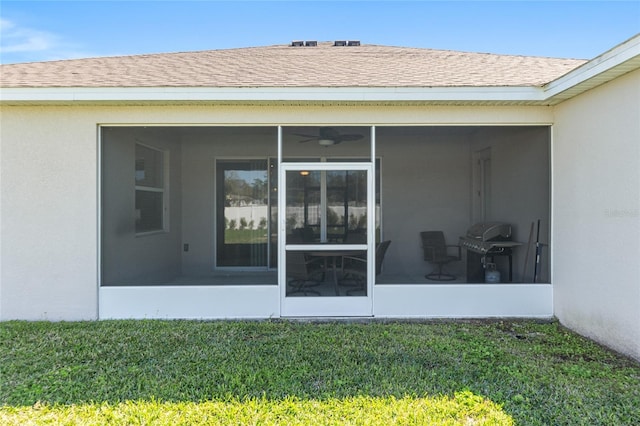 view of exterior entry featuring stucco siding, a yard, and roof with shingles