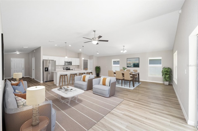 living area featuring ceiling fan, baseboards, light wood-style floors, and vaulted ceiling