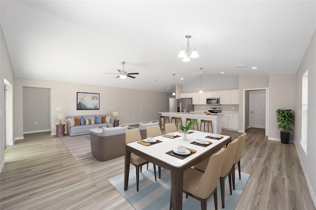 dining room featuring vaulted ceiling, ceiling fan with notable chandelier, light wood-type flooring, and baseboards