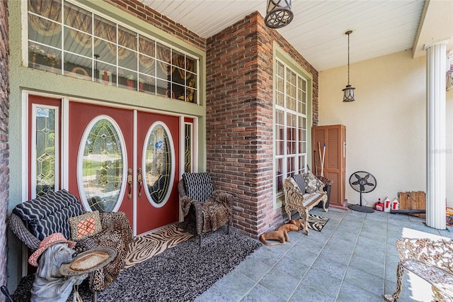 doorway to property with stucco siding, brick siding, and a porch