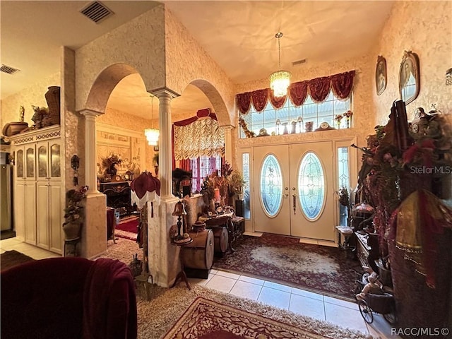 tiled foyer entrance featuring decorative columns, arched walkways, visible vents, and wallpapered walls