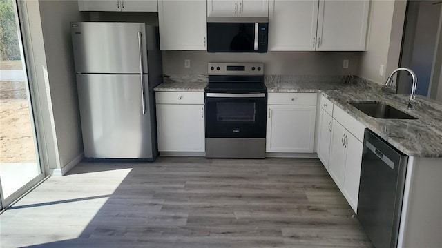 kitchen featuring light stone countertops, light wood-type flooring, stainless steel appliances, white cabinetry, and a sink