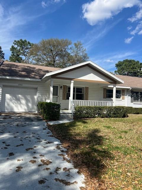 ranch-style house featuring aphalt driveway, an attached garage, covered porch, and a front lawn