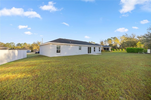 rear view of house featuring a lawn, fence, and stucco siding