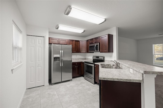 kitchen with light tile patterned floors, a peninsula, a sink, stainless steel appliances, and light countertops