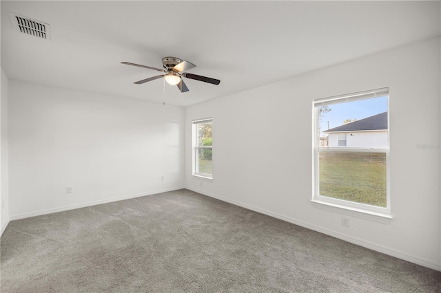 carpeted spare room with visible vents, baseboards, and a ceiling fan