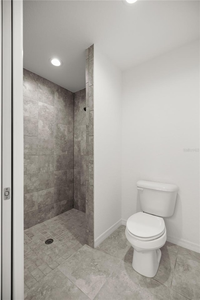 full bathroom with a tile shower, toilet, and baseboards