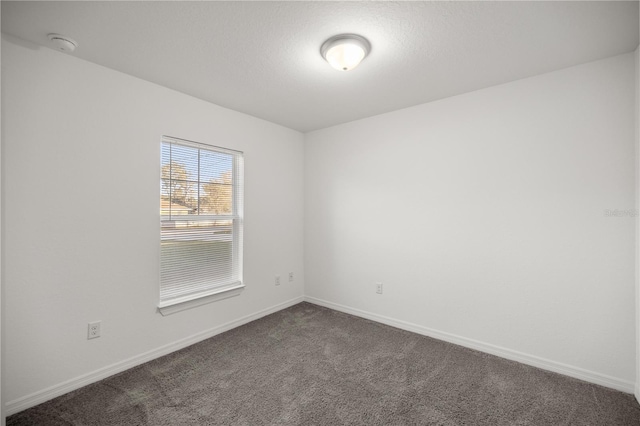 empty room featuring dark carpet and baseboards