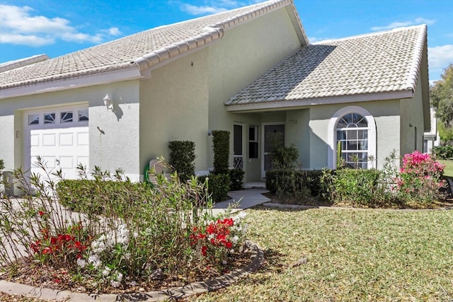 view of front of house with a tile roof, an attached garage, a front lawn, and stucco siding