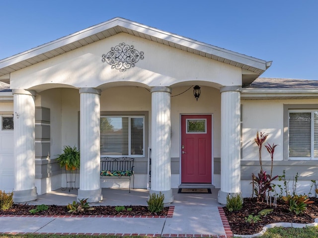 view of exterior entry featuring stucco siding, a porch, and roof with shingles