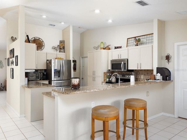 kitchen featuring visible vents, decorative backsplash, a peninsula, a kitchen breakfast bar, and stainless steel appliances