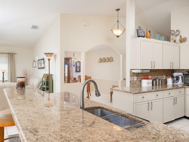 kitchen featuring tasteful backsplash, lofted ceiling, light stone counters, white cabinets, and a sink