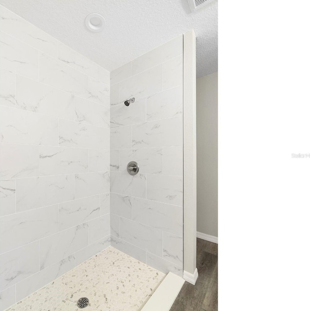 bathroom with a textured ceiling, baseboards, and tiled shower