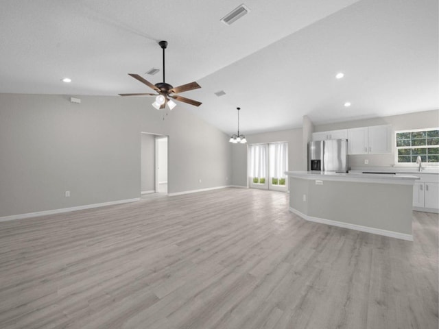 unfurnished living room featuring ceiling fan with notable chandelier, baseboards, vaulted ceiling, light wood-type flooring, and visible vents