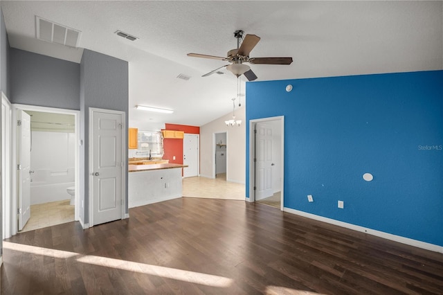 unfurnished living room with lofted ceiling, wood finished floors, ceiling fan with notable chandelier, and visible vents