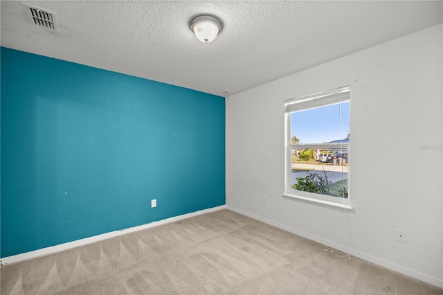 spare room featuring visible vents, carpet flooring, a textured ceiling, and baseboards