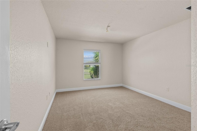 spare room with visible vents, a textured ceiling, carpet floors, baseboards, and a textured wall