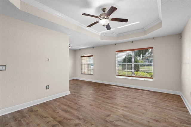 empty room with a raised ceiling, wood finished floors, baseboards, and ornamental molding