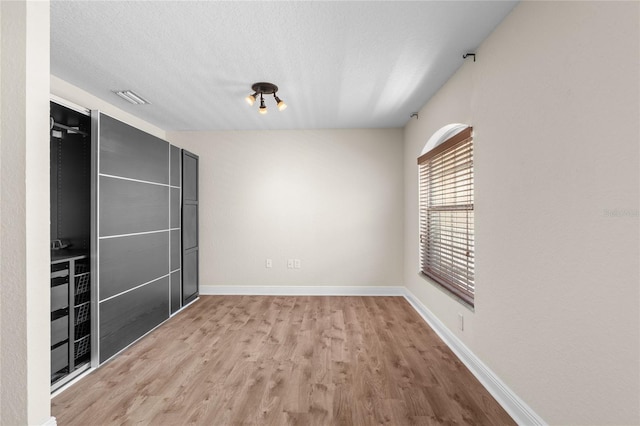 spare room with a textured ceiling, wood finished floors, visible vents, and baseboards