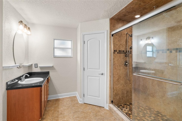 full bath with vanity, baseboards, a stall shower, a textured ceiling, and a textured wall