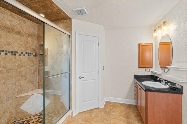 full bath featuring visible vents, a textured ceiling, a shower stall, baseboards, and vanity