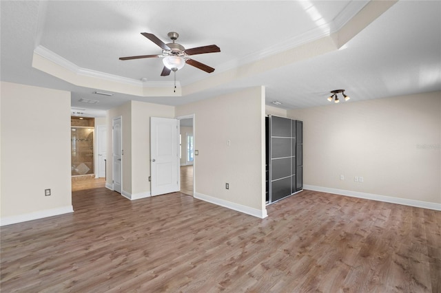 interior space featuring baseboards, ornamental molding, wood finished floors, a raised ceiling, and a ceiling fan