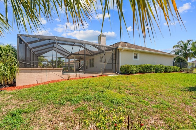 back of property featuring stucco siding, a yard, glass enclosure, and a chimney