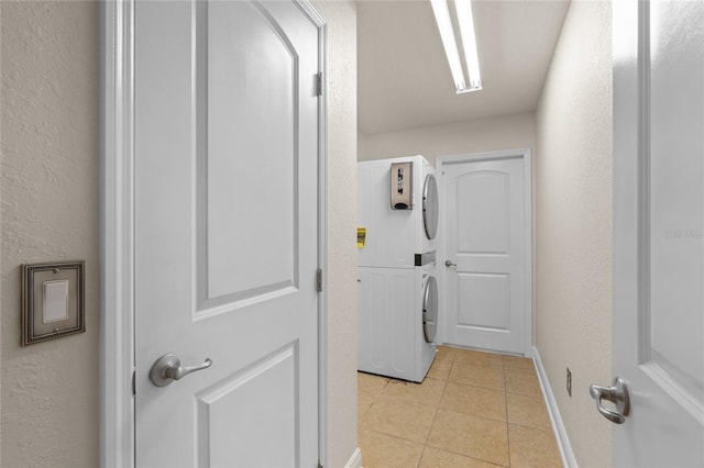 clothes washing area with light tile patterned floors, stacked washer and dryer, laundry area, and a textured wall