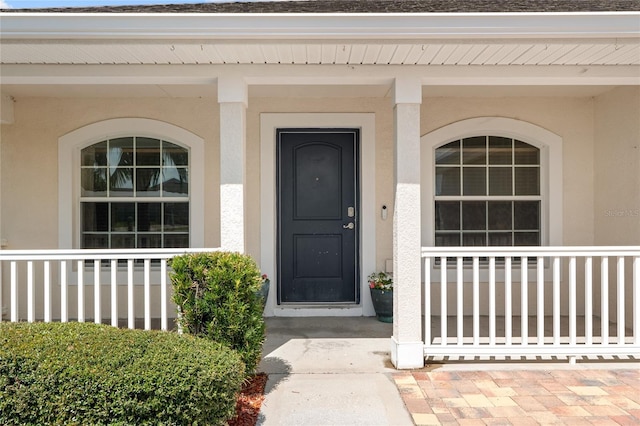 doorway to property with covered porch and stucco siding